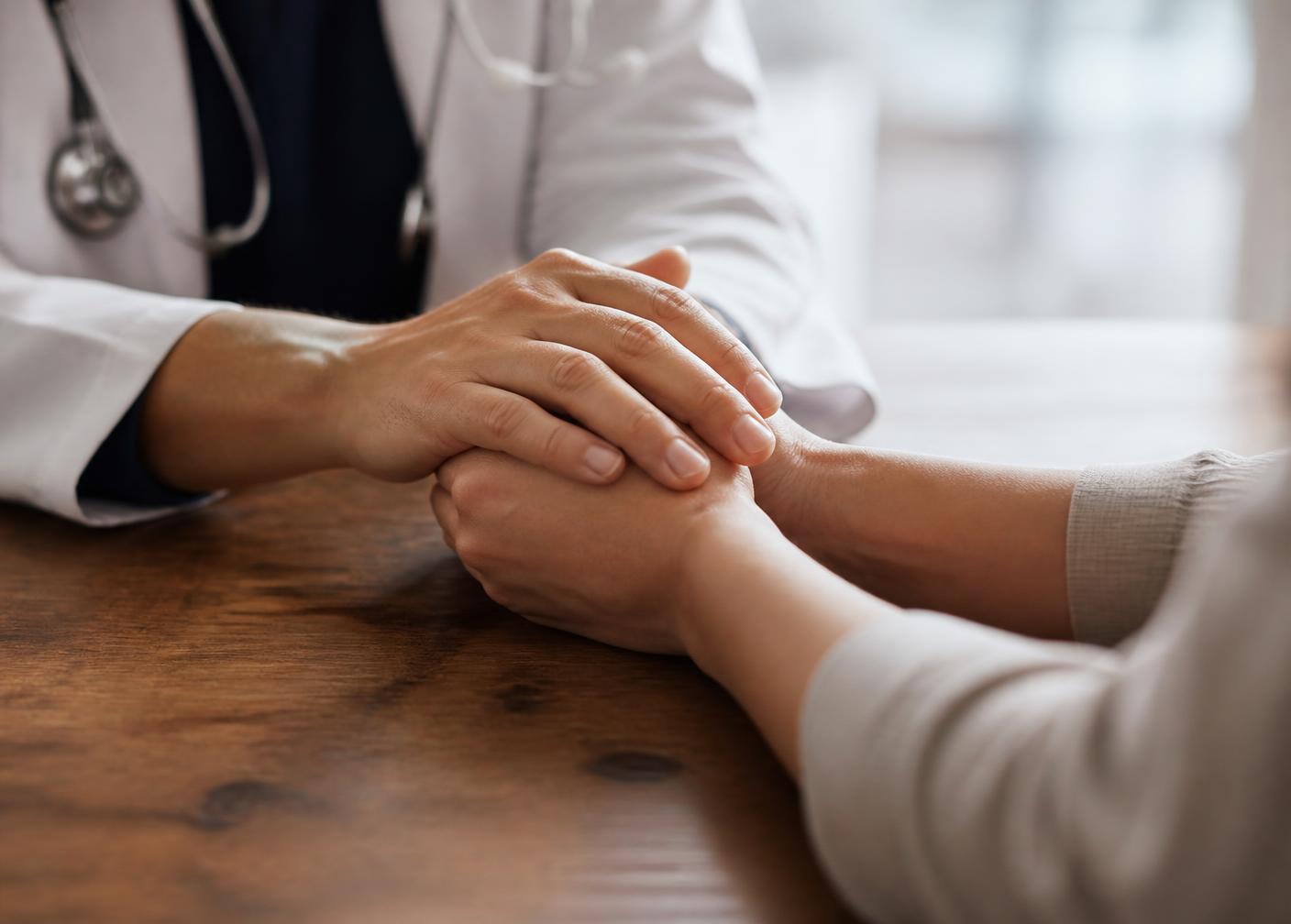 A clinician's hands resting gently over a patient's hands